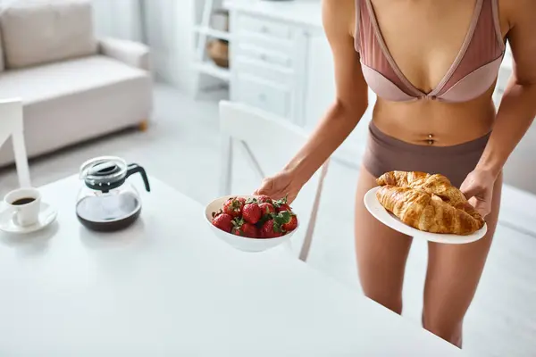 Cropped african american woman in lingerie holding plates with croissants and strawberries — Stock Photo
