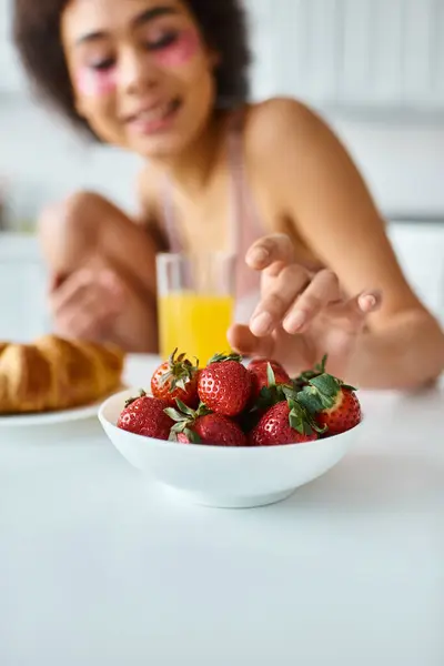 Blurred african american woman reaching fresh strawberries during breakfast in kitchen — Stock Photo