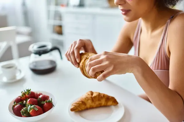 Cropped happy african american woman holding freshly baked croissant during breakfast — Stock Photo