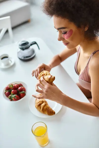 Happy african american woman holding freshly baked croissant during breakfast in kitchen, top view — Stock Photo