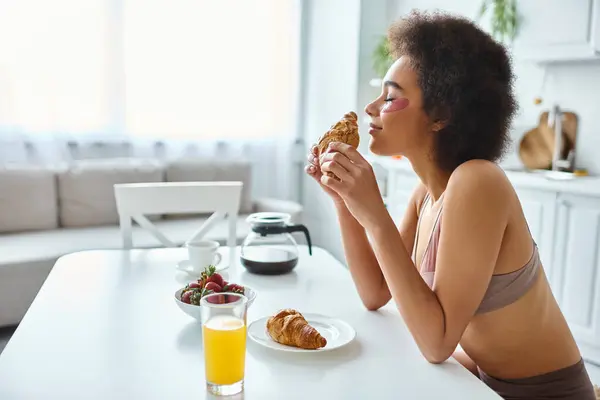 Sorridente donna afroamericana che tiene croissant appena sfornato durante la colazione in cucina — Foto stock