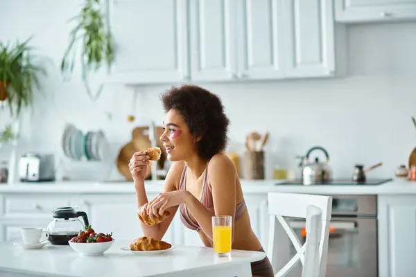 Donna afro-americana positiva che tiene croissant appena sfornato durante la colazione in cucina — Foto stock