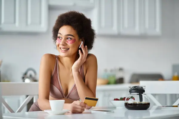 Щаслива афроамериканка в навушниках з патчами під очима покупки в Інтернеті з кредитною карткою — стокове фото