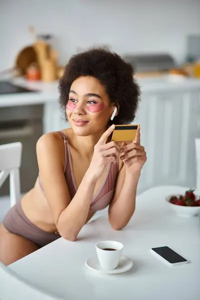 Sonriente mujer afroamericana en auriculares con parches bajo los ojos comprando con tarjeta de crédito - foto de stock
