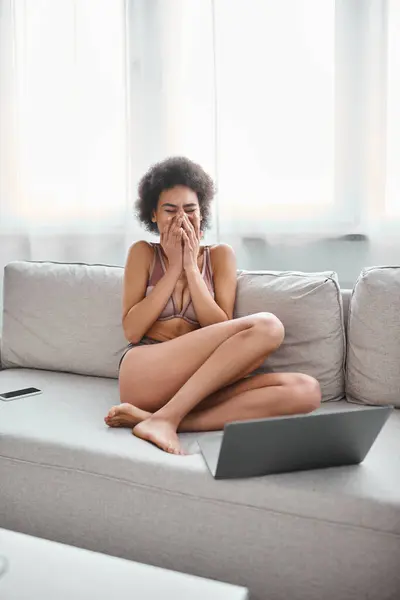 Mulher americana africana em lingerie sentado no sofá e rindo enquanto assiste filme no laptop — Fotografia de Stock