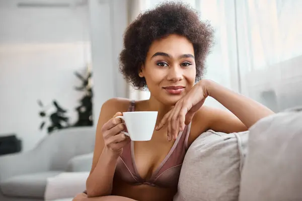 Glückliche afrikanisch-amerikanische Frau in Dessous mit Tasse Kaffee und Blick in die Kamera — Stockfoto