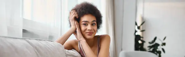 Retrato de jovem e encaracolado afro-americano mulher em lingerie olhando para câmera em casa, banner — Fotografia de Stock