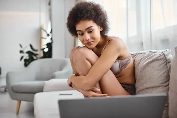 African american woman in lingerie sitting on sofa and watching movie on laptop, weekend vibes — Stock Photo