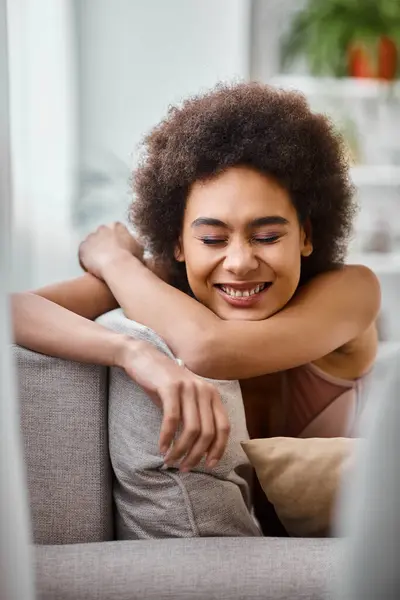 Glücklich afrikanisch-amerikanische Frau mit lockigem Haar entspannt auf der Couch in Dessous, lächelnd mit geschlossenen Augen — Stockfoto