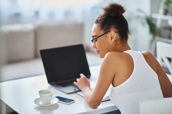 Frisé afro-américaine femme dans des lunettes de travail de la maison sur son ordinateur portable, entrepreneur — Photo de stock