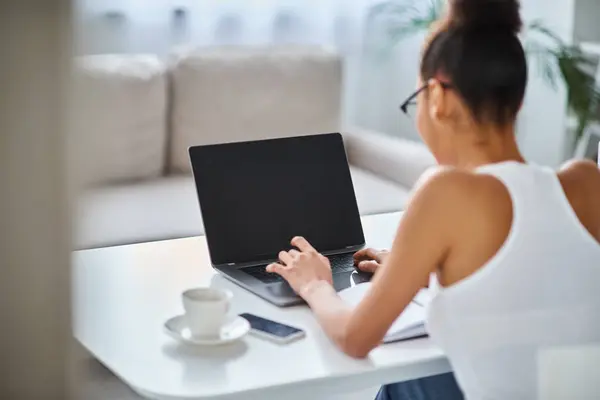 Jeune et frisée afro-américaine dans des lunettes de travail de la maison sur son ordinateur portable, entrepreneur — Photo de stock