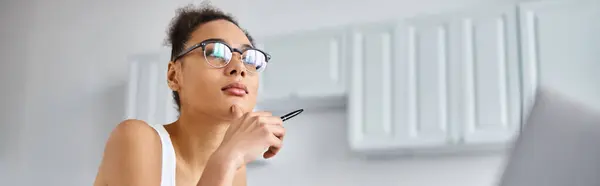Donna afroamericana pensierosa in occhiali che lavora da casa da remoto e tiene la penna, banner — Foto stock