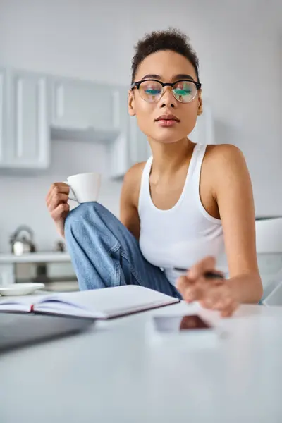 Curly african american woman in glasses working from home and reaching blurred smartphone on desk — Stock Photo