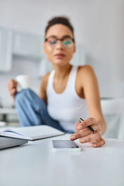 Blurred african american woman in glasses working from home and using smartphone on desk — Stock Photo