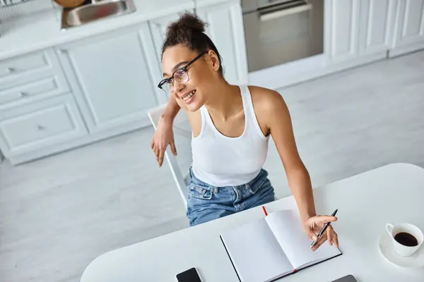 Top view of happy african american woman with pen sitting at desk with cup of coffee and notebook — Stock Photo