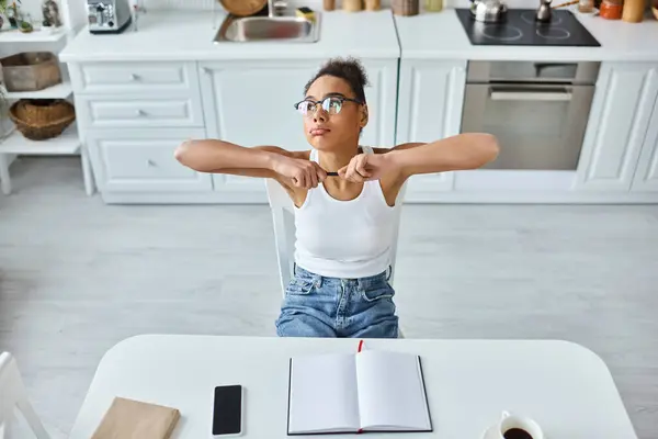 Vista dall'alto di stanca donna afroamericana con penna seduta alla scrivania con tazza di caffè e notebook — Foto stock