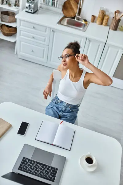 Von oben: verträumte afrikanisch-amerikanische Frau mit Stift sitzt am Schreibtisch mit Tasse Kaffee und Notizbuch — Stockfoto