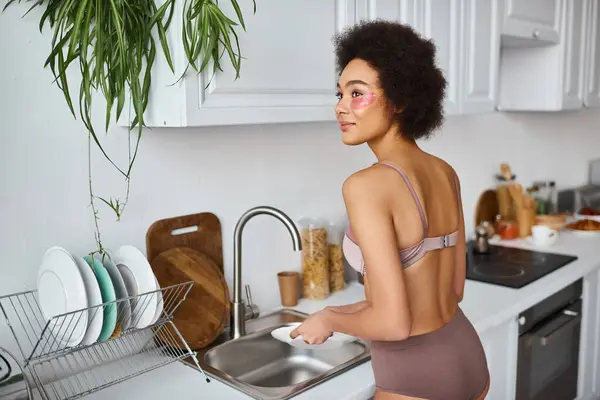 Мрійлива афроамериканська жінка в білизні з плямами для очей пральна машина з губкою на кухні — стокове фото
