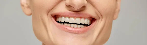 Обрезанное знамя счастливой женщины, излучающей радостную и здоровую улыбку на сером фоне, белые зубы — стоковое фото