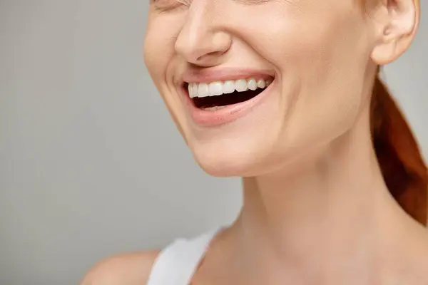 Cropped view of happy woman in tank top exuding joyful and healthy smile on grey background — Stock Photo
