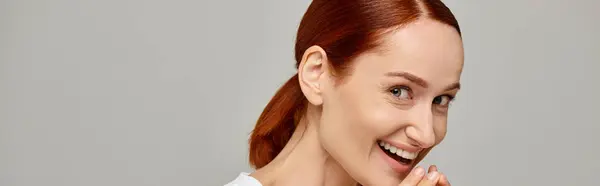 Astonished and redhead woman in white tank top laughing a grey background, radiant smile banner — Stock Photo