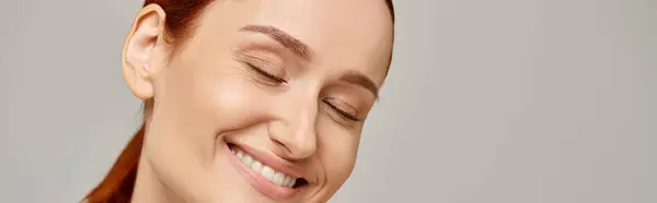 Femme heureuse et rousse en débardeur blanc souriant avec les yeux fermés sur fond gris, bannière — Photo de stock