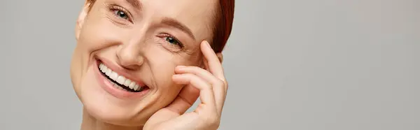 Banner of cheerful and redhead woman looking at camera on grey background, healthy smile — Stock Photo