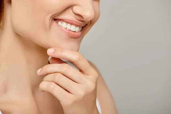 Cropped view of woman with healthy smile touching radiant skin on grey background, close up — Stock Photo