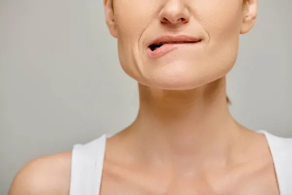 Обрізаний вид на стомлену жінку в білому баку зверху кусає губу, втілюючи занепокоєння на сірому фоні — стокове фото