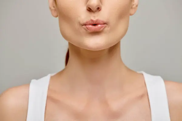 Vista recortada de la mujer en sus 30 puckering labios sobre un fondo gris neutro, soplando - foto de stock