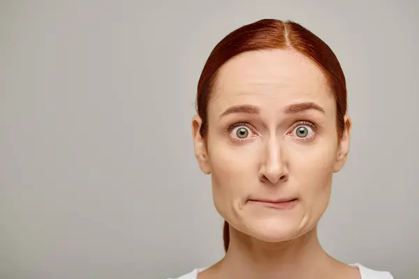 Redhead and worried woman in white tank top embodying concern on grey background, concerned face — Stock Photo