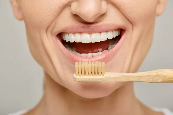Cropped shot of happy woman in 30s with white healthy teeth holding a bamboo toothbrush, open mouth — Stock Photo