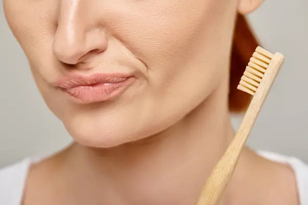 Cropped shot of concerned woman in 30s holding a bamboo toothbrush on grey background — Stock Photo