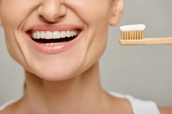 Ausgeschnittene Ansicht einer fröhlichen Frau, die eine Zahnbürste mit Zahnpasta in der Hand hält und in die Kamera lächelt — Stockfoto