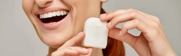 Cropped banner of positive redhead woman holding dental floss case and smiling on grey background — Stock Photo