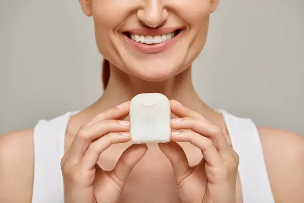 Cropped view of positive redhead woman holding dental floss case and smiling on grey background — Stock Photo