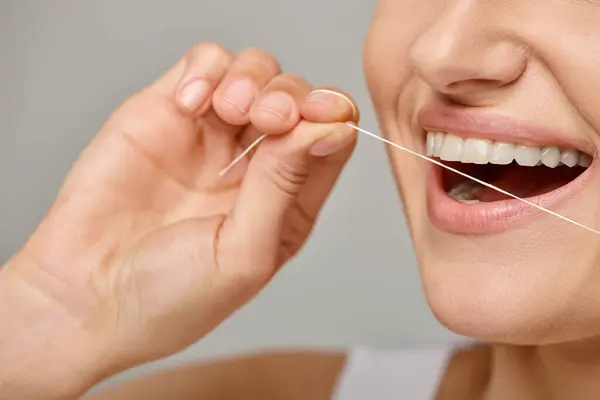 Excité femme cultivée tenant fil dentaire et souriant sur fond gris, la promotion de l'hygiène buccodentaire — Photo de stock