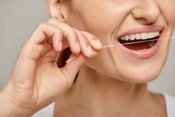 Gestutzte Frau mit Zahnseide und Lächeln auf grauem Hintergrund, die Mundhygiene fördert — Stockfoto