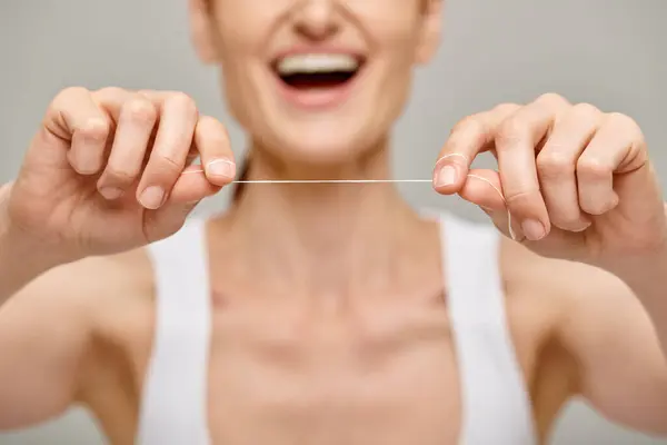 Enfoque en hilo dental sobre fondo gris, vista recortada de la mujer feliz que promueve la higiene bucal - foto de stock