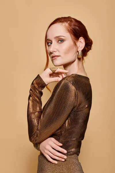 Redhead woman in her 30s posing in elegant attire with golden accessories on beige backdrop — Stock Photo
