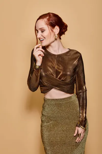 Happy redhead woman in her 30s posing in elegant attire and golden accessories on beige backdrop — Stock Photo
