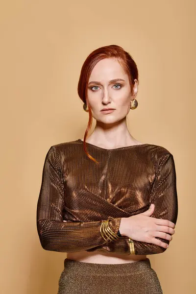 Redhead woman in her 30s posing in trendy outfit with golden accessories on beige backdrop, portrait — Stock Photo