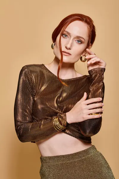 Pelirroja de 30 años posando con elegante atuendo y accesorios dorados con las manos cerca de la cara - foto de stock