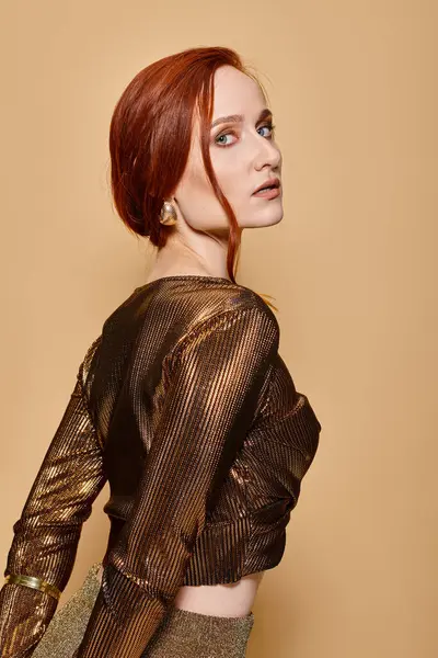 Portrait of confident redhead woman in 30s posing in trendy attire and golden accessories on beige — Stock Photo