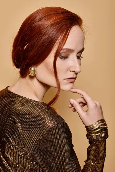 Portrait of charming redhead woman in 30s posing in trendy attire and golden accessories on beige — Stock Photo