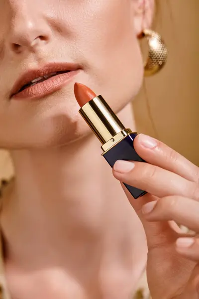 Abgeschnittene Ansicht einer Frau mit goldenen Ohrringen mit Lippenstift auf beigem Hintergrund, Schönheitskonzept — Stockfoto