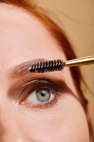 Abgeschnittene Ansicht einer Frau mit grünen Augen, die Mascara auf beigem Hintergrund aufträgt, Make-up und Schönheit — Stockfoto