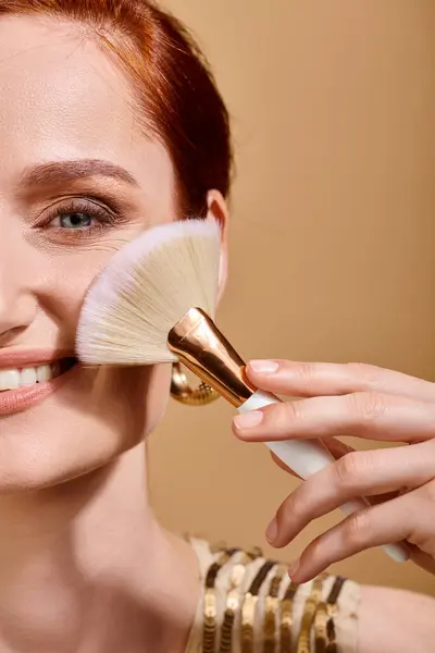 Cropped view of happy woman in gold earring applying bronzer with makeup brush on beige background — Stock Photo