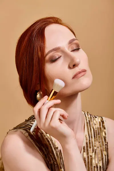 Rothaarige Frau mit goldenem Ohrring mit Make-up-Pinsel auf beigem Hintergrund — Stockfoto