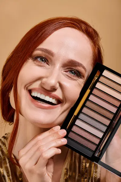 Close up of happy woman holding eye shadow palette on beige background, makeup advertisement — Stock Photo